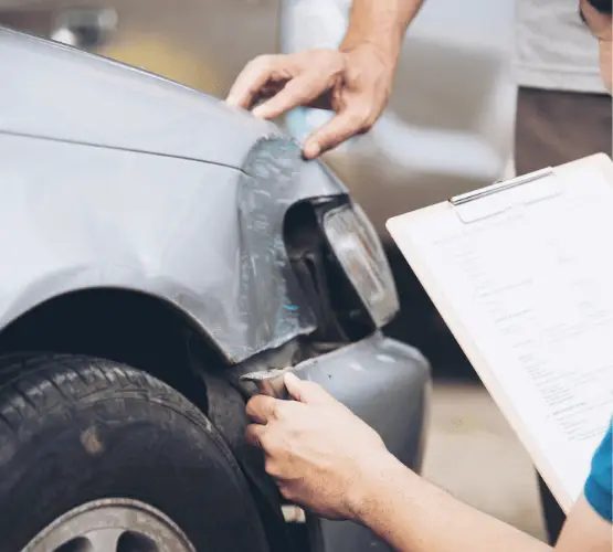 Auto body technician inspecting front-end collision damage on a vehicle.
